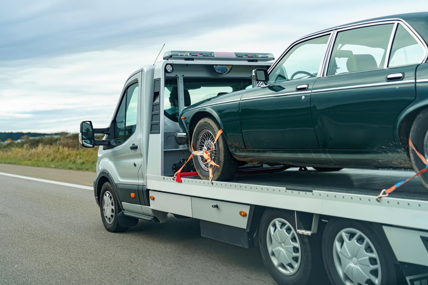 Older sedan strapped down on a flatbed tow truck