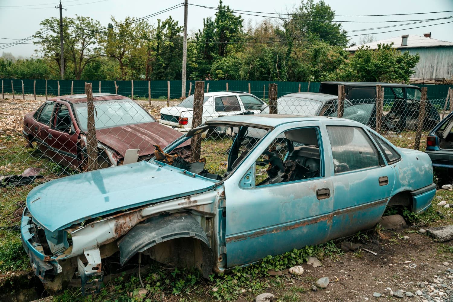 Wrecked sedan shell sitting in a fenced junkyard